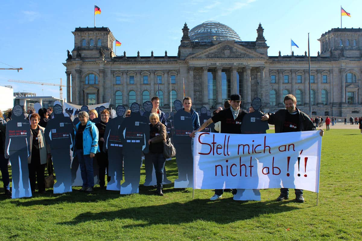 Menschen halten ein Plakat mit der Aufschrift "Stell mich an und nicht ab!".